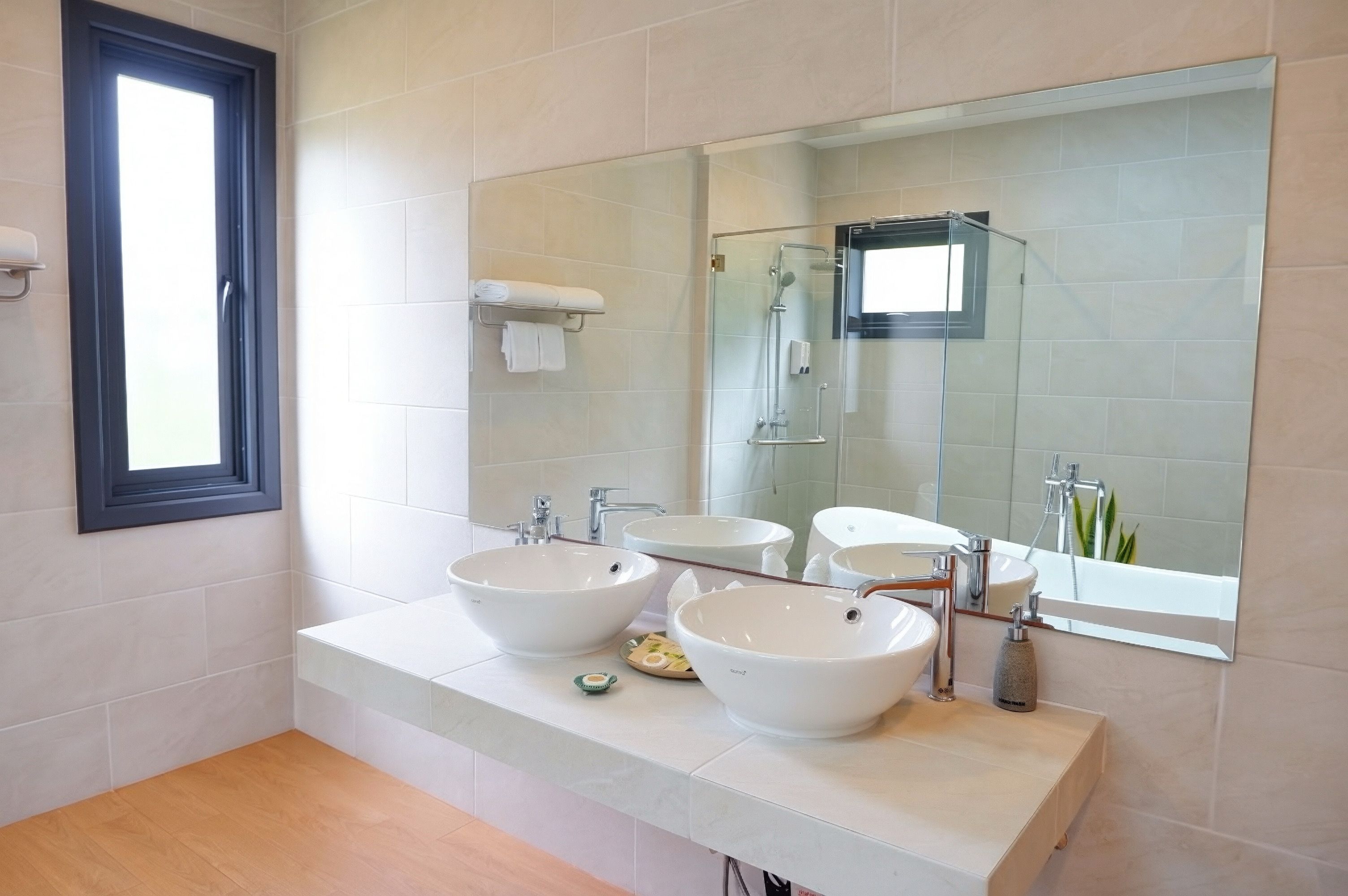 A modern bathroom with two sinks, a large mirror, and a shower.