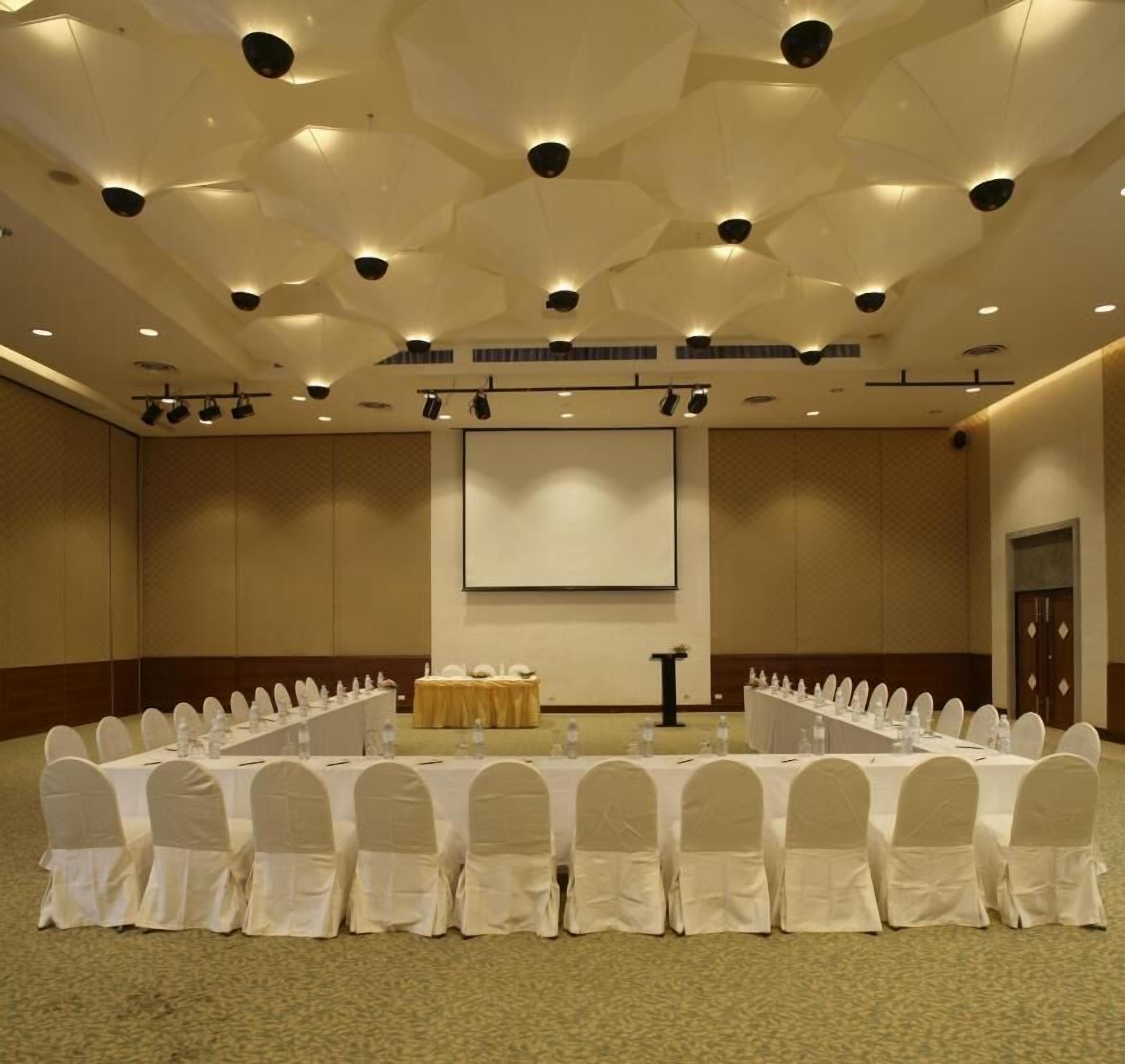 A conference room with a long table, white chairs, and a projector screen.