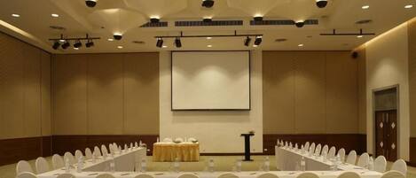 A conference room with a long table, white chairs, and a projector screen.