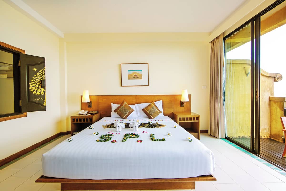 A hotel room with a large bed, two bedside tables, a nightstand, a framed picture on the wall, and a sliding glass door to the balcony.