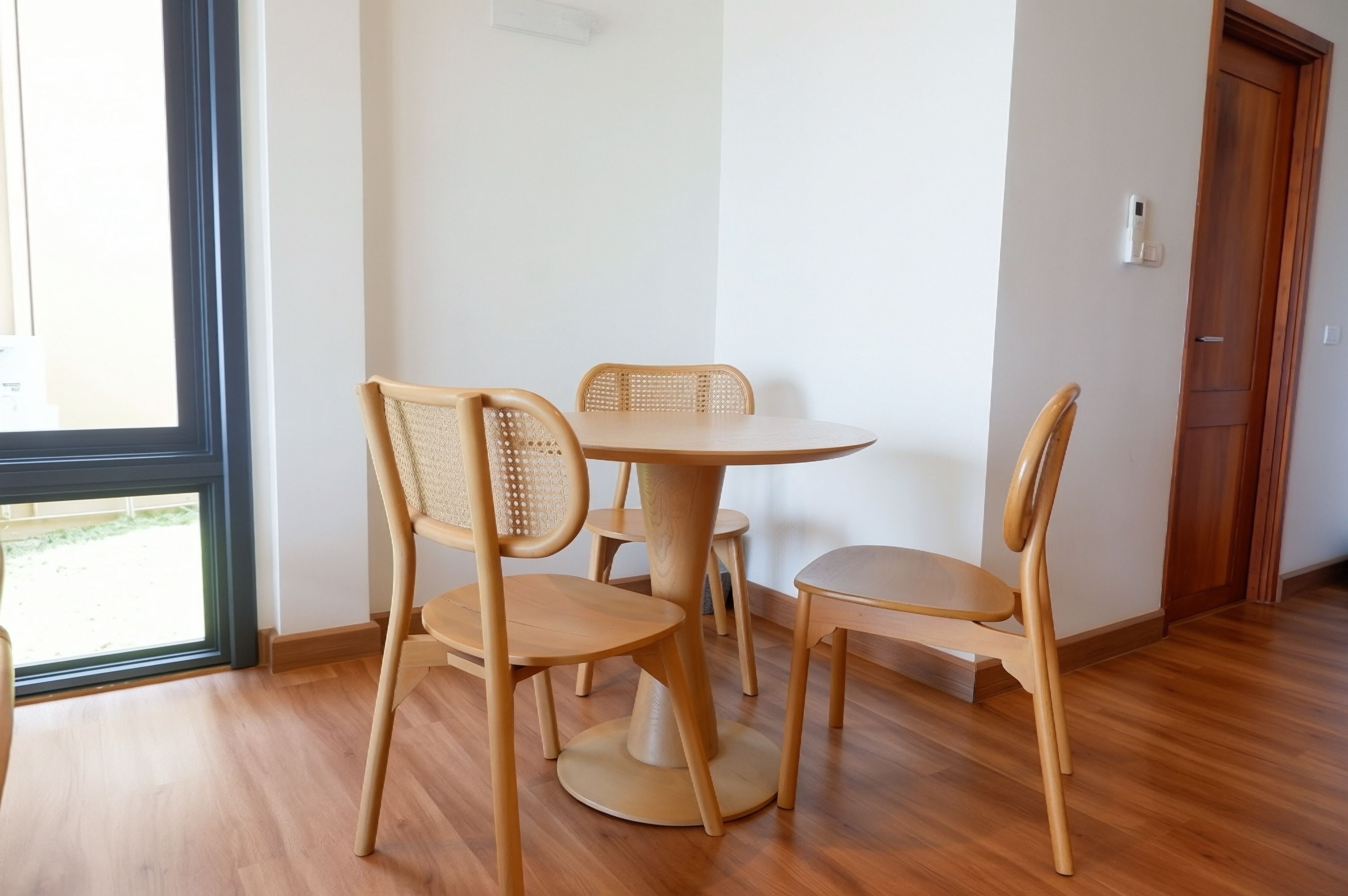 A room with a round wooden table and four chairs, a wooden floor, a door, and a window.