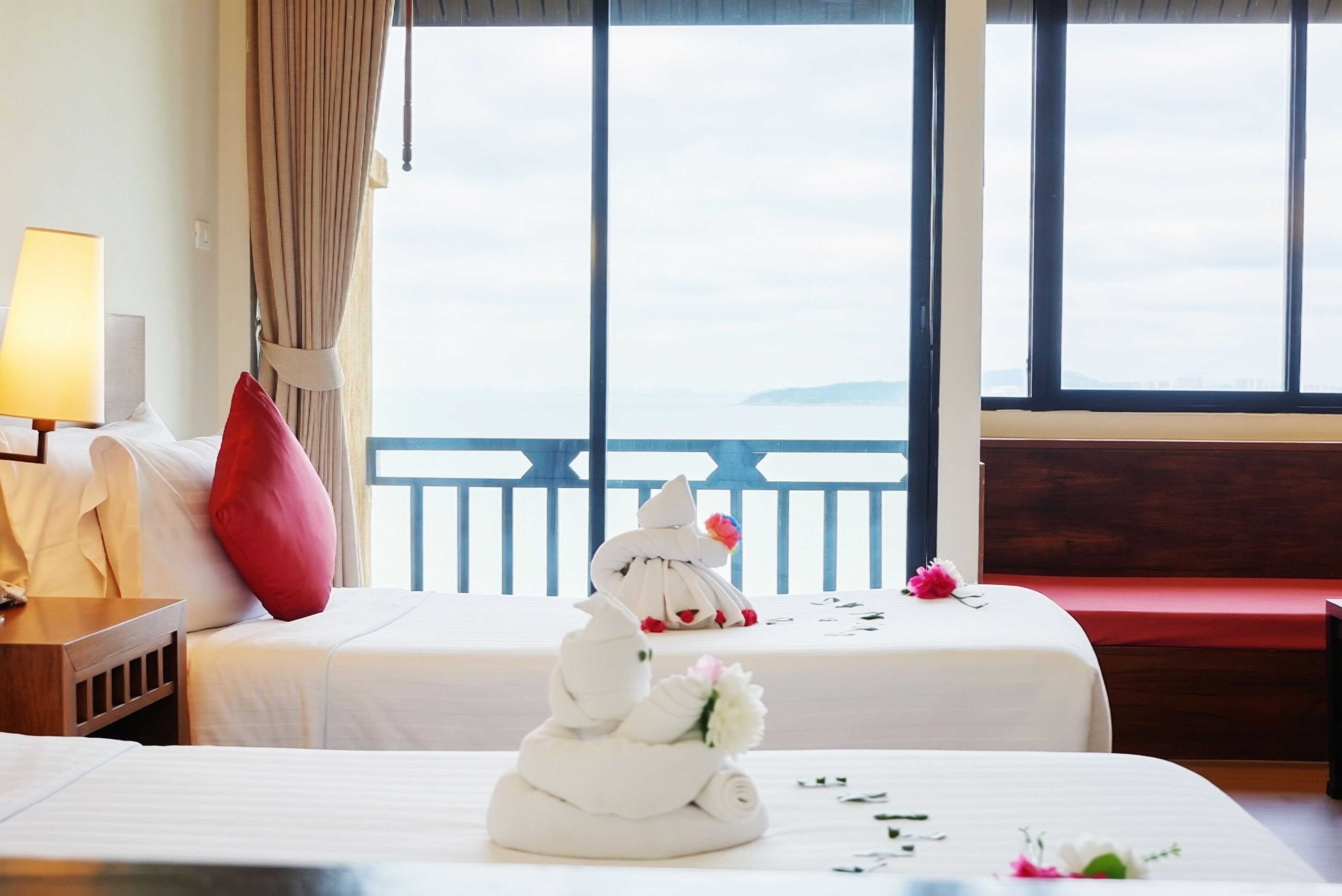 A hotel room with two beds, a view of the sea, and a balcony with a railing.