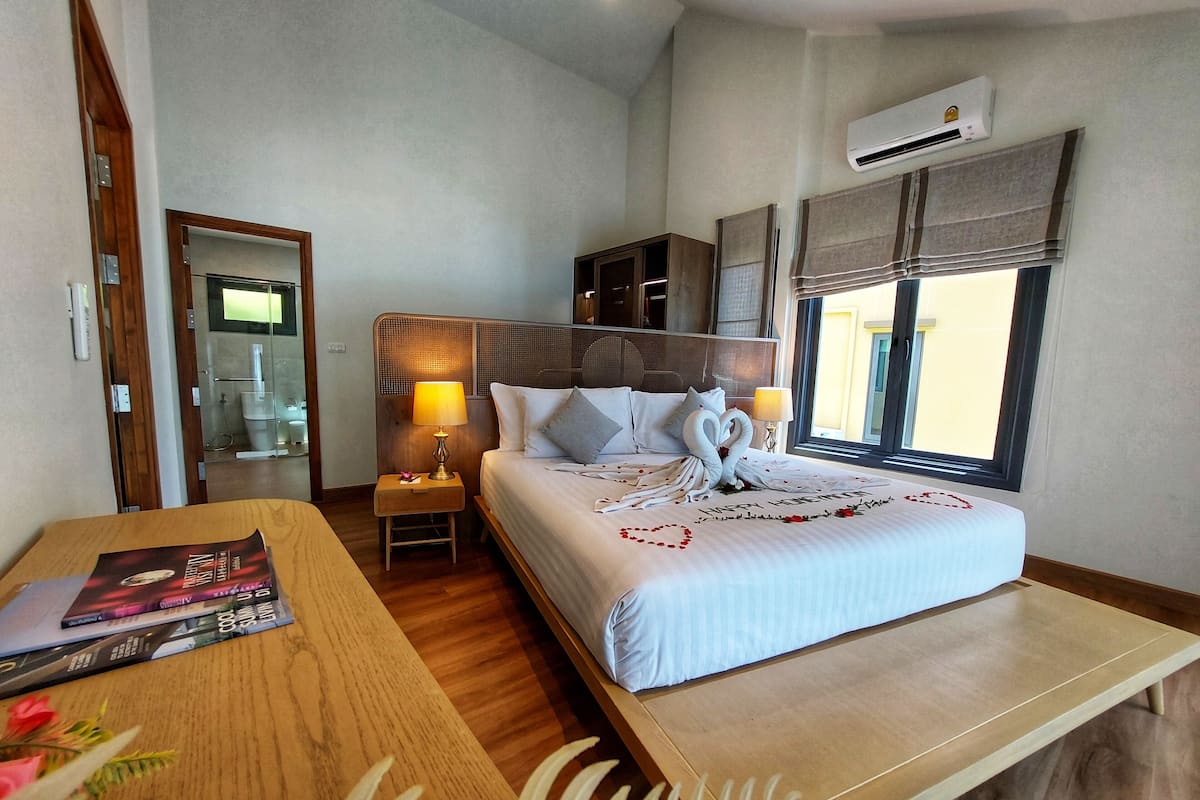 A hotel room with a bed, bedside tables, a desk, and an air conditioning unit.