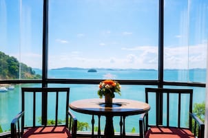 Una mesa con un florero y sillas orientadas a un ventanal con vista a un cuerpo de agua y tierra distante.