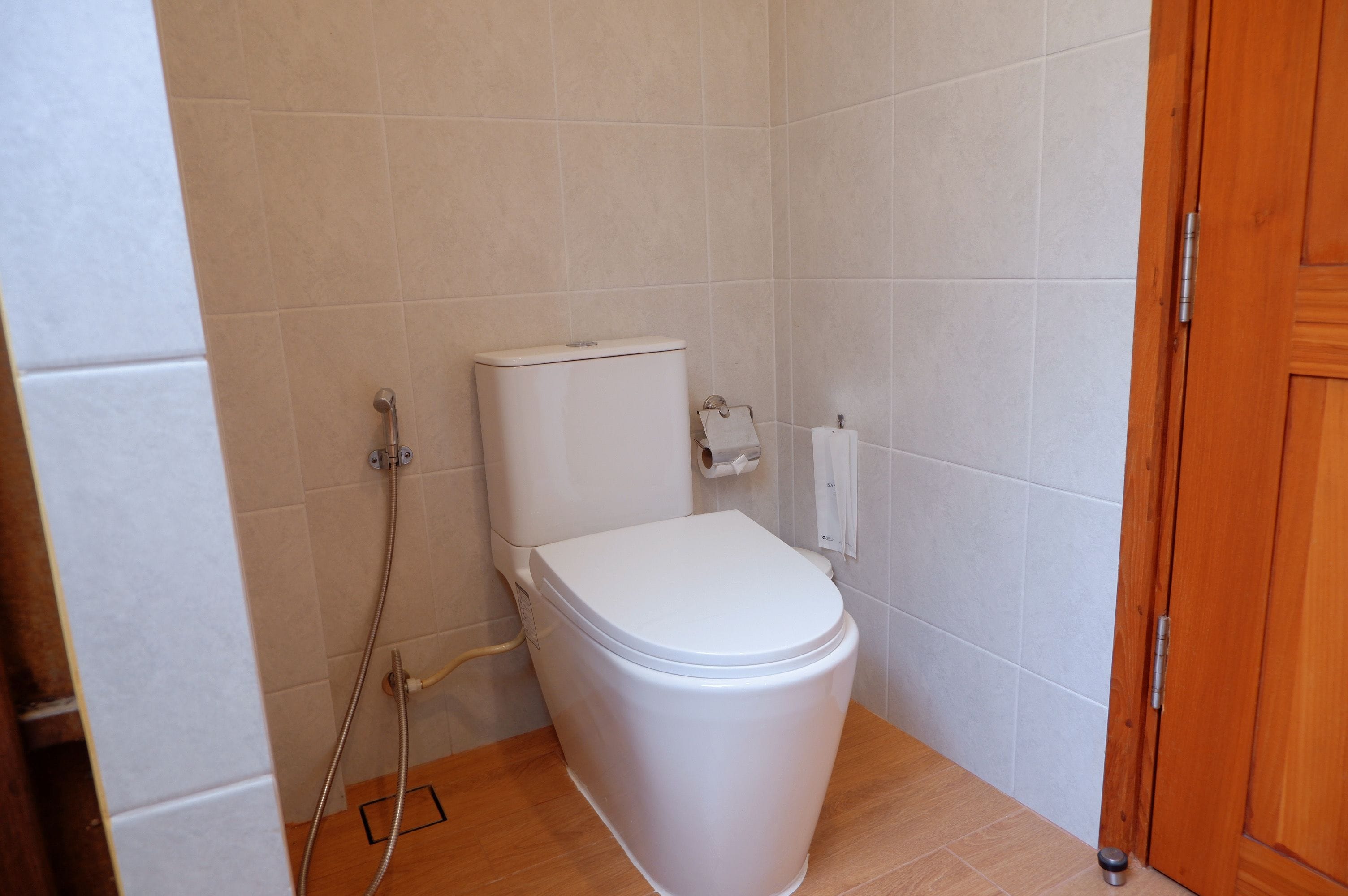 Un baño pequeño y limpio con inodoro blanco, ducha y puerta de madera.