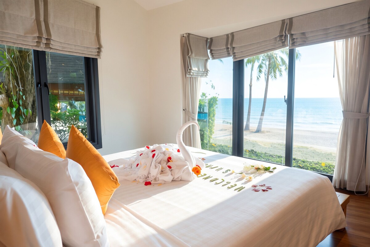 A hotel room with a bed, a swan-shaped pillow, and a view of the beach.