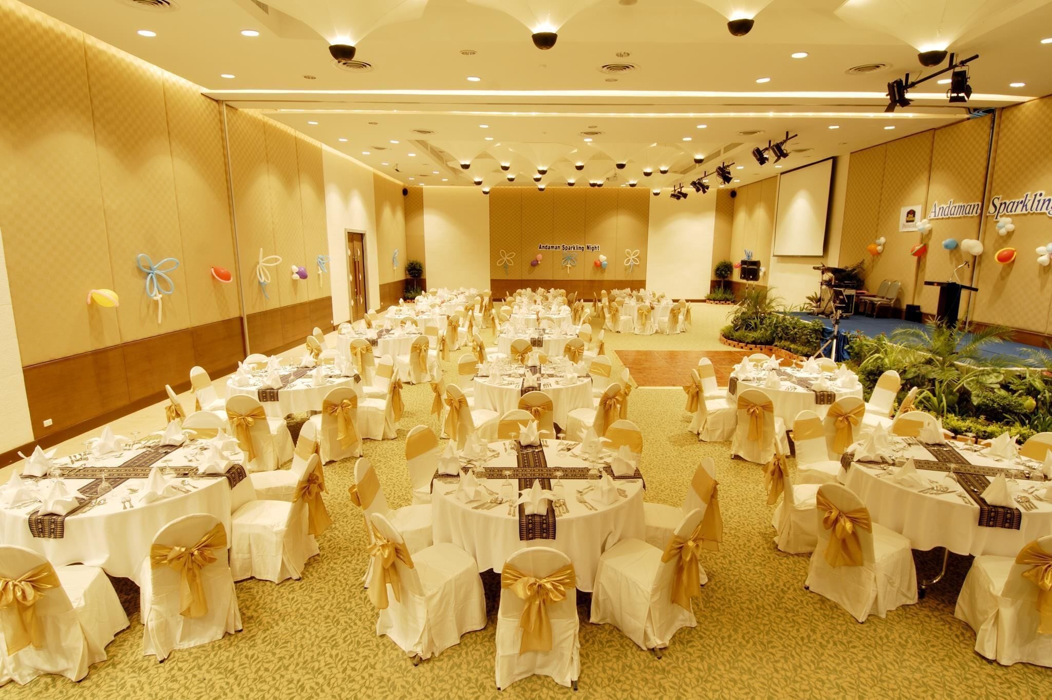 Salão de banquetes com mesas redondas dispostas para um evento formal, apresentando um layout uniforme e uma área de palco.