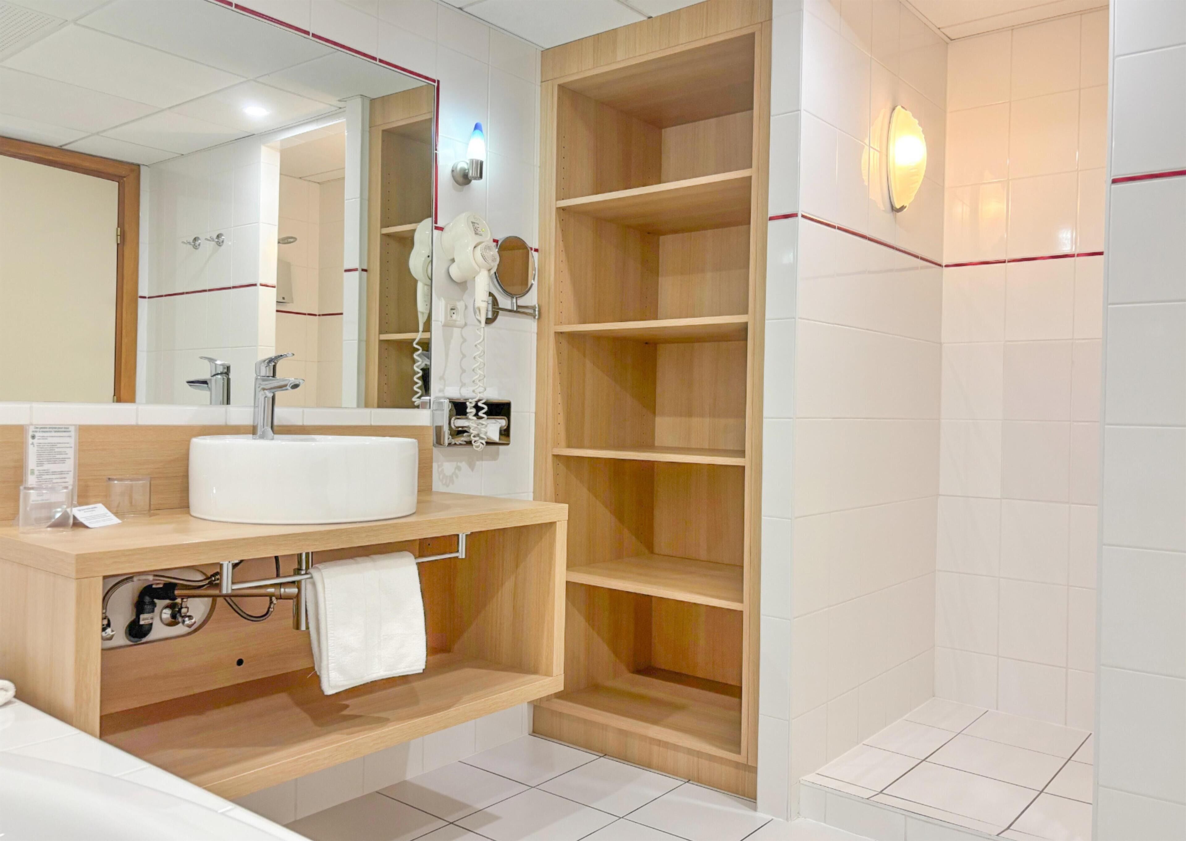 A modern bathroom with a white sink, mirror, and wooden shelves.