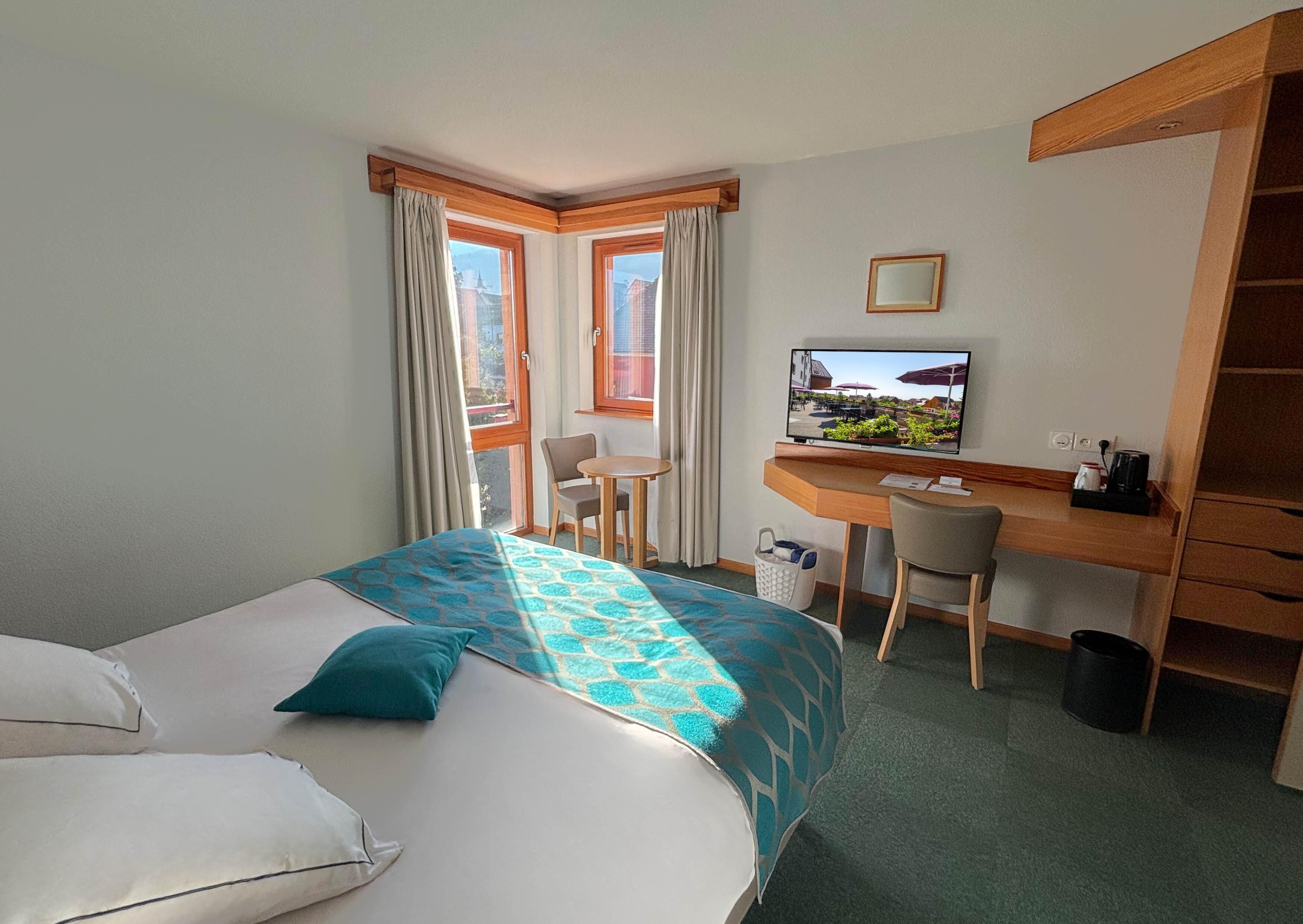 Ein Hotelzimmer mit einem Bett, einem Schreibtisch, einem Sessel, einem Fernseher und Blick ins Freie.