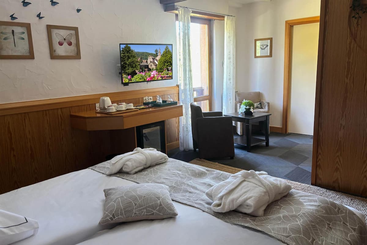 Ein Hotelzimmer mit einem Bett, einem Schreibtisch mit Fernseher, einem Sessel, einem kleinen Tisch und einer Tür.