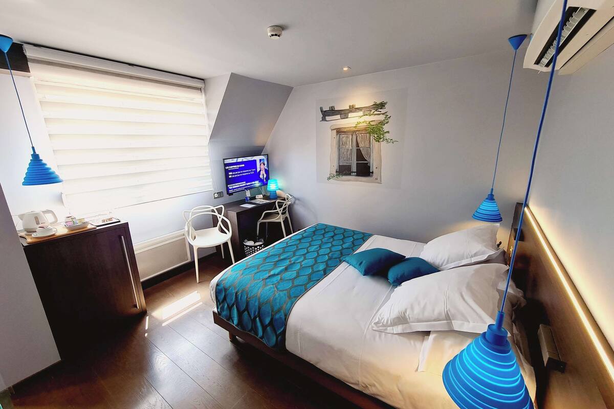 Ein modernes Hotelzimmer mit einem großen Bett, einem Schreibtisch mit Computer, einem Stuhl und einem kleinen Fenster.