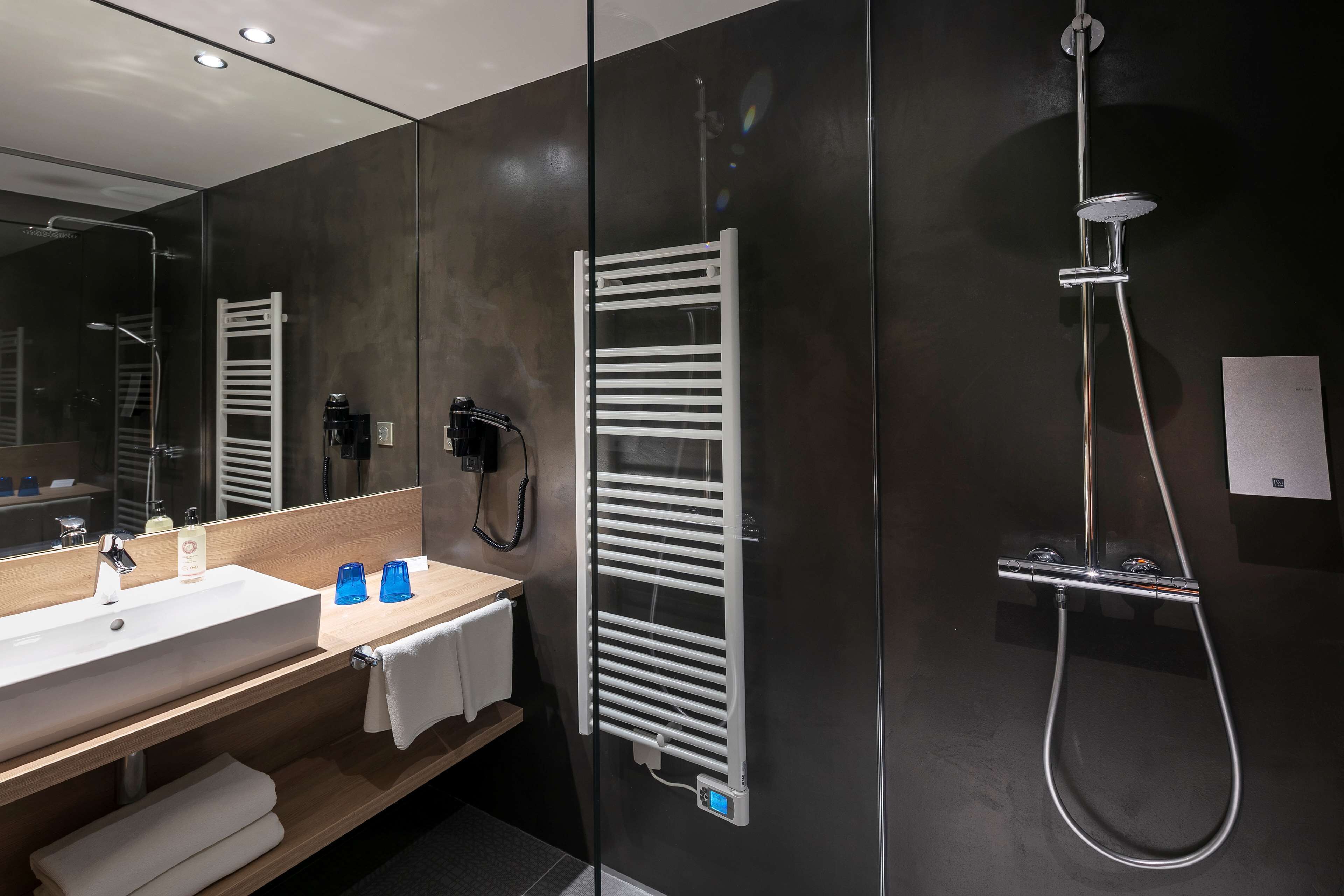 Een moderne badkamer met een grote spiegel, een witte wastafel, een handdoekrek, een verwarmde handdoekhouder en een douche met een handdouche.