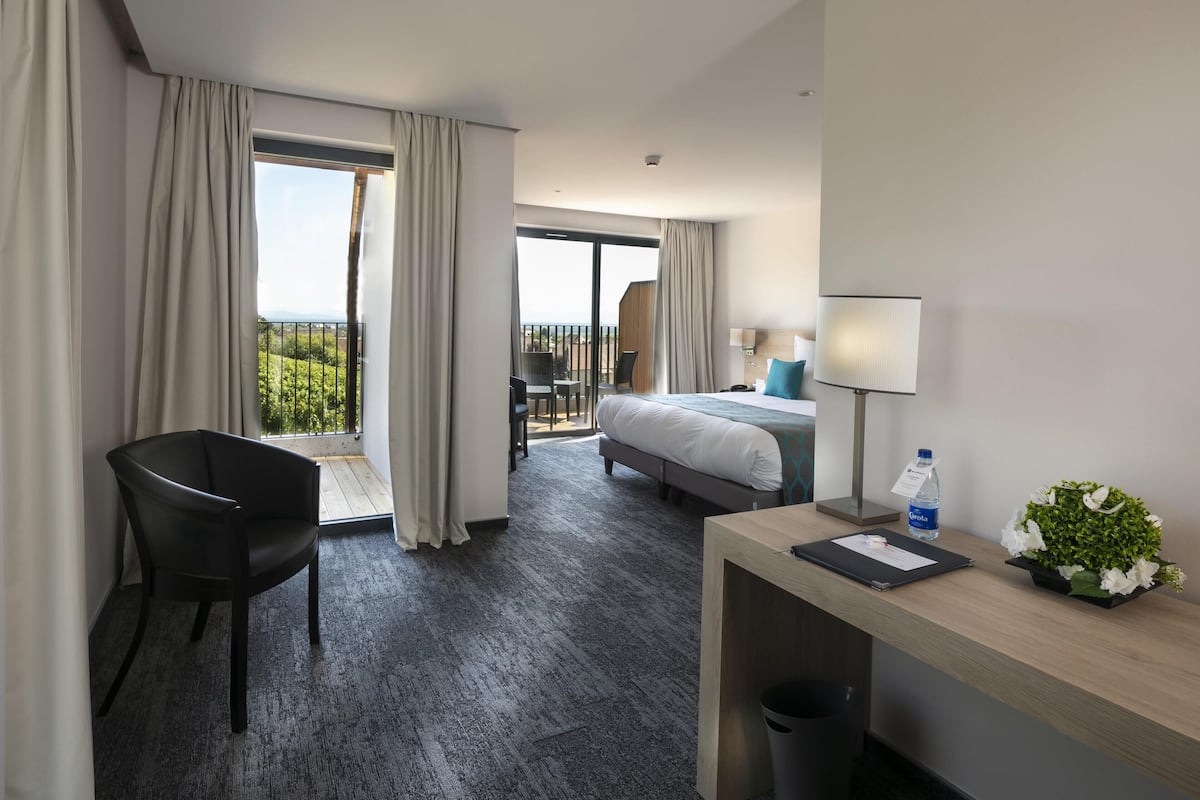 Ein Hotelzimmer mit Bett, Schreibtisch, Stuhl, Balkon und Blick auf Grünflächen.
