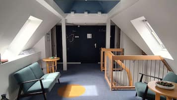 Ein Zimmer mit schrägverdeckter Decke, einer Holztreppe, einem blauen Sofa, einem kleinen runden Tisch und einer Tür mit einem Schild.