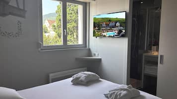 Ein Hotelzimmer mit Bett, Wand-Fernseher, Fenster mit Blick auf Gebäude und Bäume sowie einer Duschkabine.