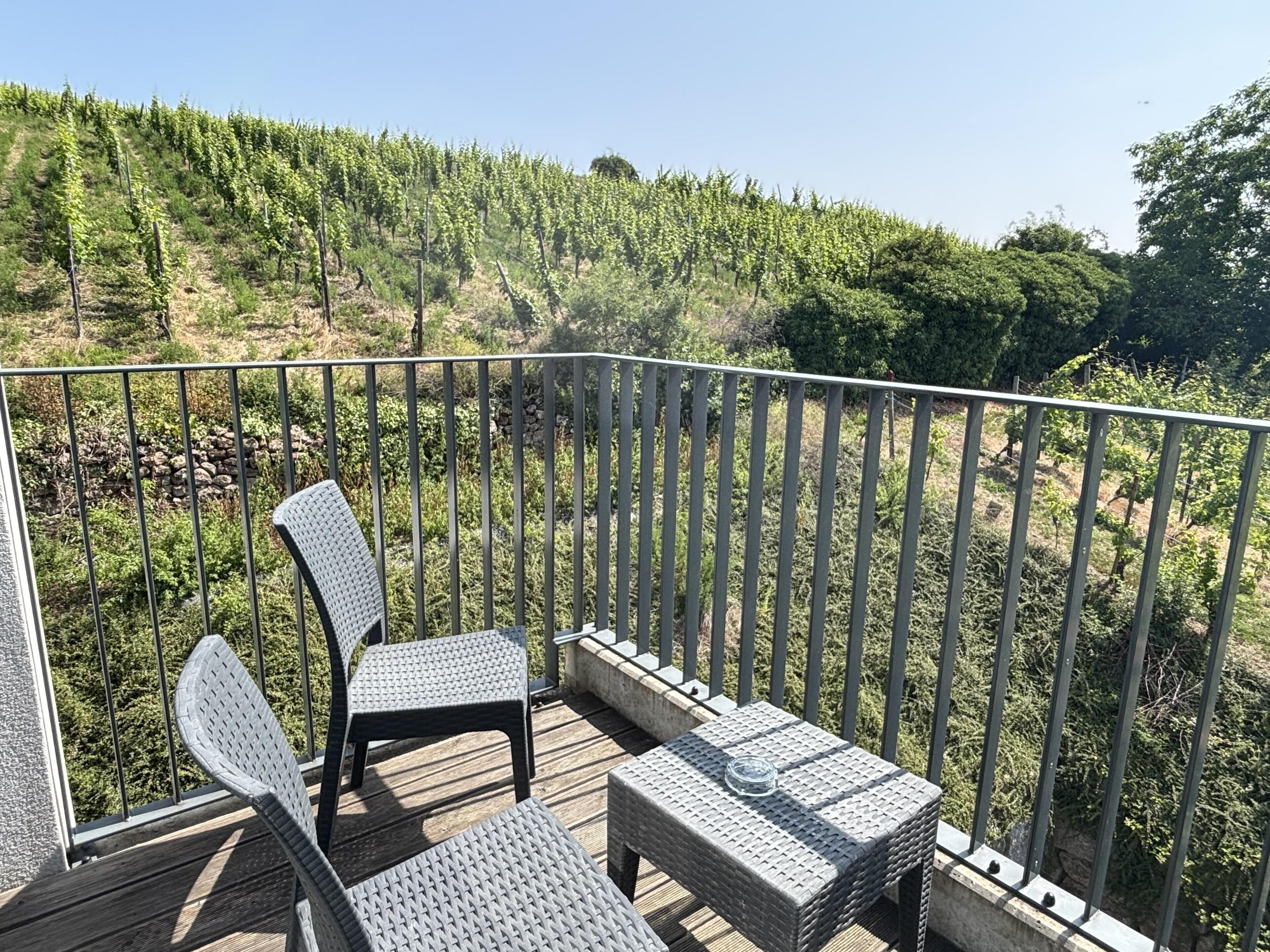 A balcony with wicker furniture and a view of a vineyard.