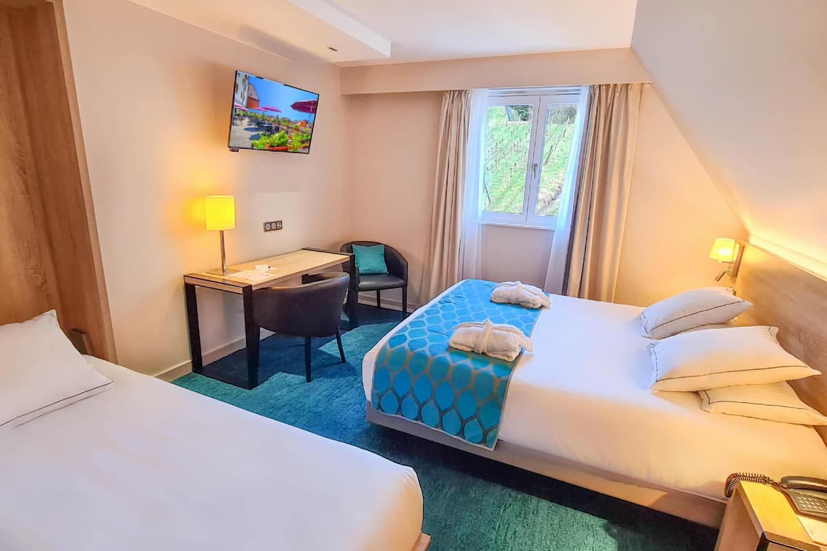 Ein Hotelzimmer mit zwei Betten, einem Schreibtisch, einem Stuhl, einem Fernseher und einem Fenster mit Vorhängen.