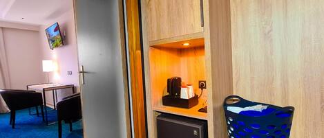 A hotel room with a desk, chair, TV, minibar, and a blue chair.