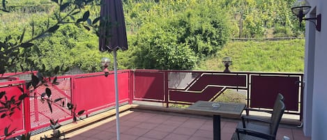 Una terraza con mesa y sillas, una valla roja y vistas a un viñedo.