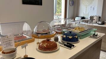 A breakfast buffet with various food items, including pastries and meats, displayed under glass covers.
