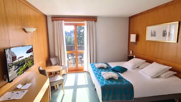 Een hotelkamer met een bed, een bureau, een stoel, een televisie en een balkon met gordijnen.