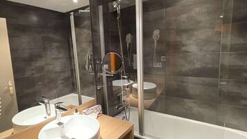 A modern bathroom with two sinks, a glass shower enclosure, and a bathtub.