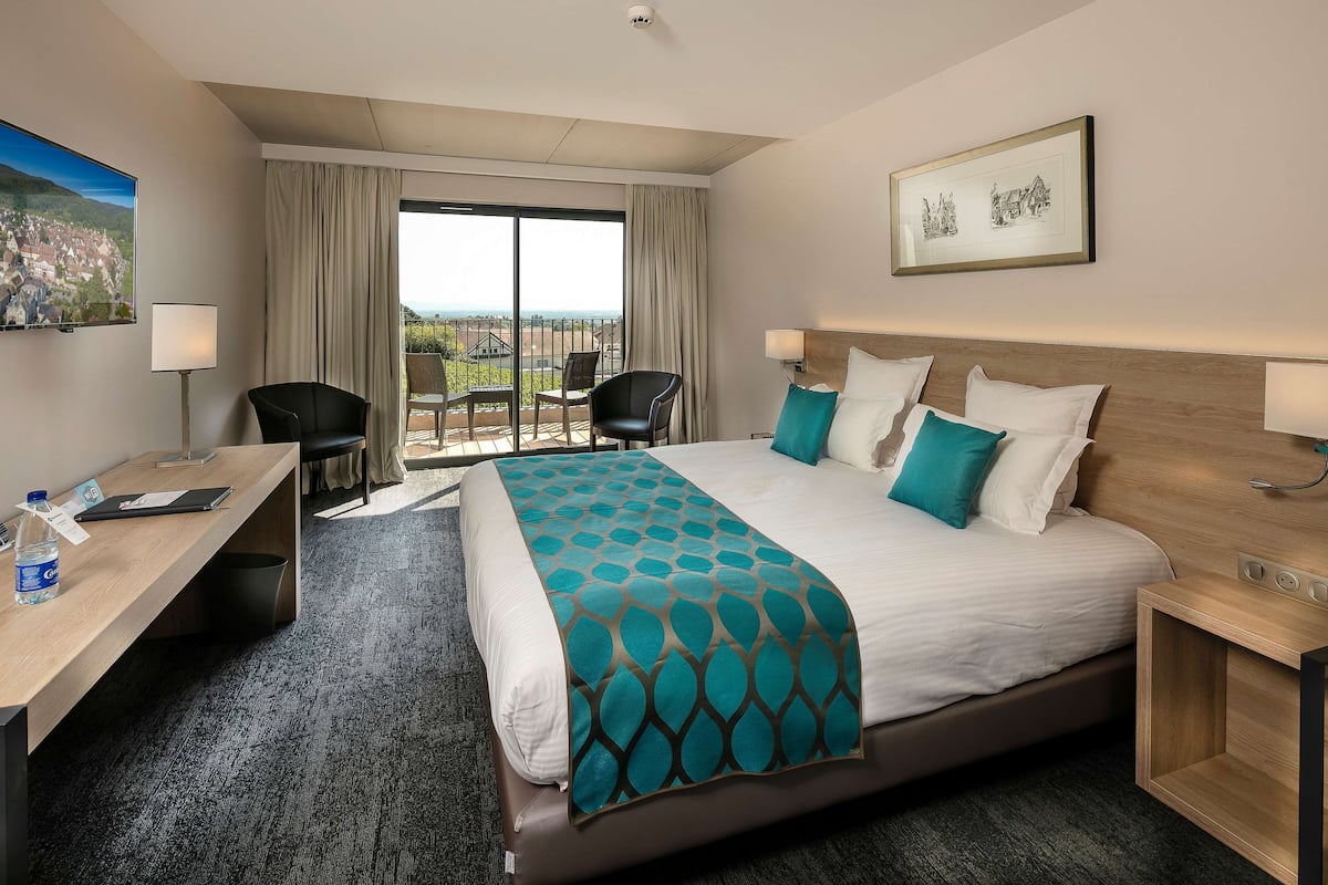 Ein Hotelzimmer mit einem großen Bett, einem Schreibtisch, einem Sessel und einem Balkon mit Blick.