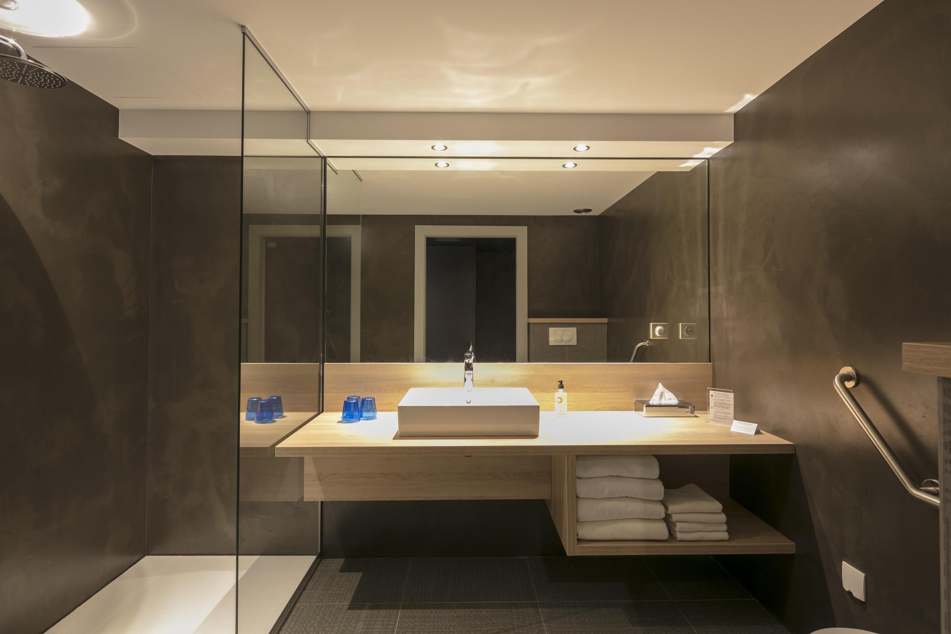 A modern bathroom with a large mirror, a sink, and a shower area.