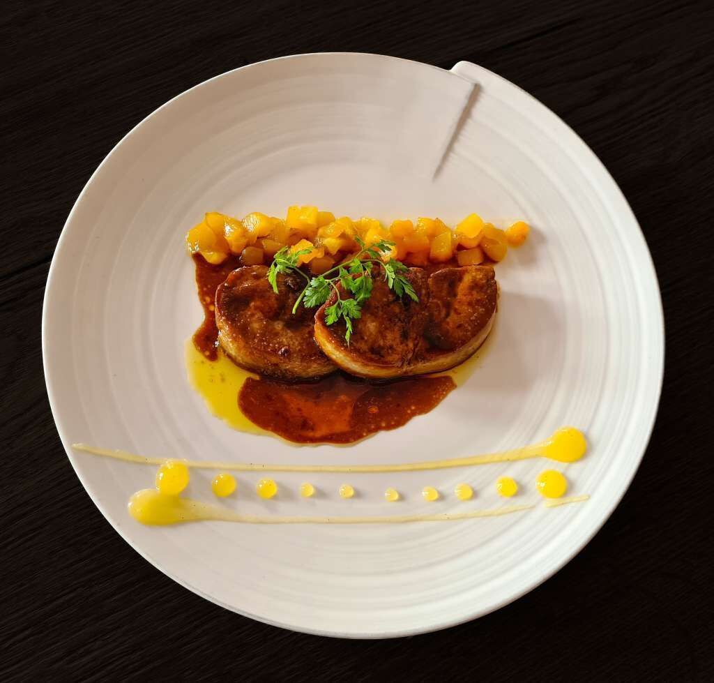 Un plato blanco con un guiso de carne, maíz y salsa, adornado con hierbas, sobre una superficie oscura.