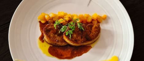 Un plato blanco con un guiso de carne, maíz y salsa, adornado con hierbas, sobre una superficie oscura.