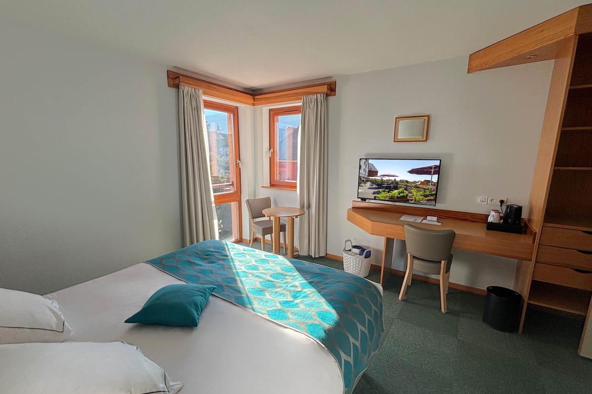 Ein Hotelzimmer mit Bett, Schreibtisch, Stuhl, Fernseher und Blick ins Freie.
