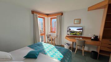 A hotel room with a bed, a desk, a chair, a television, and a view of the outdoors.