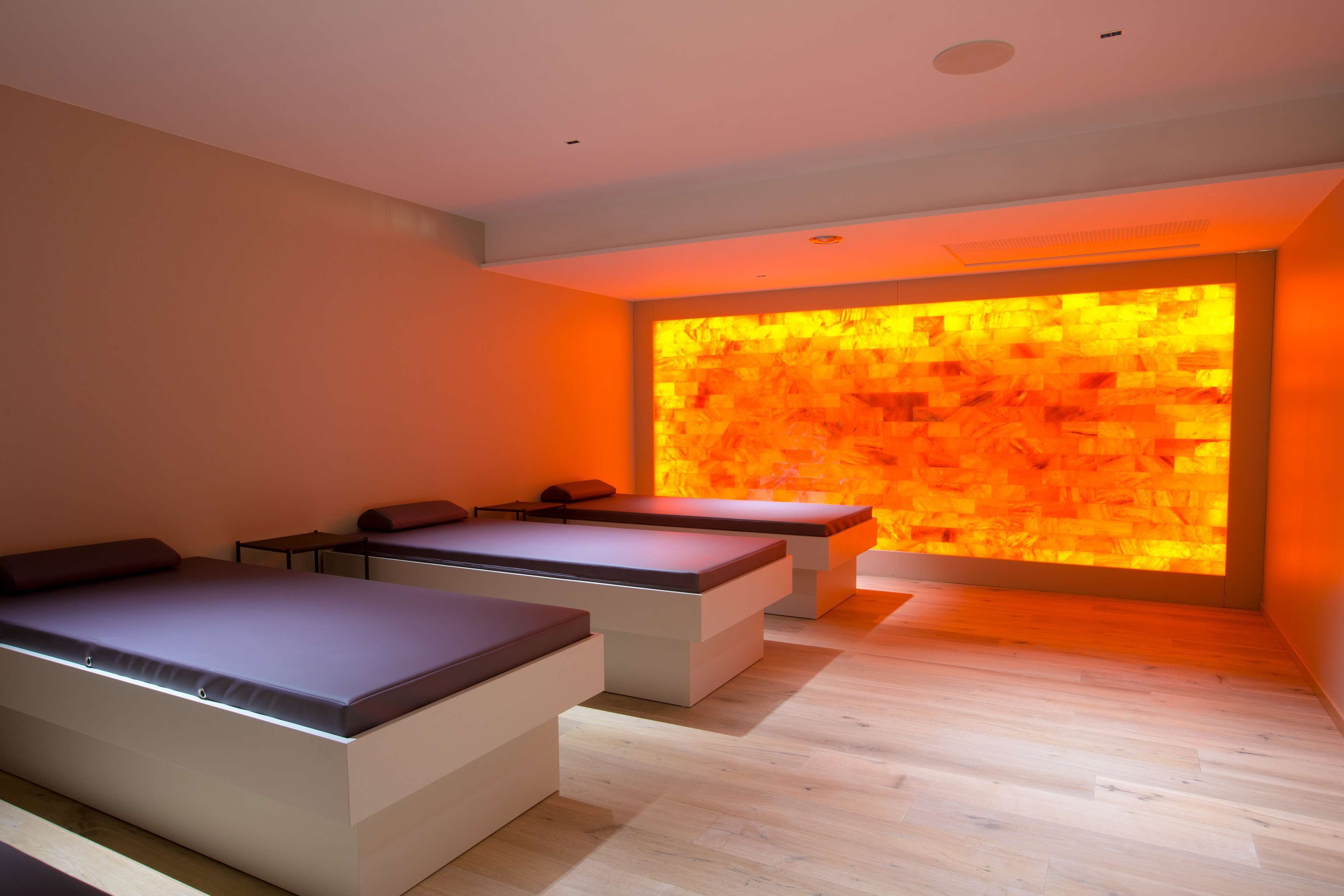 Ein moderner Wellnessraum mit einer erwärmten Steinwand, einem Massagetisch und einer Entspannungszone mit einer Bank.