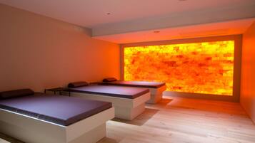 Ein moderner Wellnessraum mit einer erwärmten Steinwand, einem Massagetisch und einer Entspannungszone mit einer Bank.