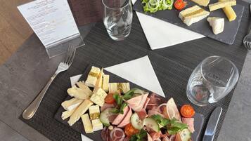 Ein Tisch mit verschiedenen Käsesorten, Wurstwaren und einem Salat, begleitet von einer Speisekarte und Gläsern.