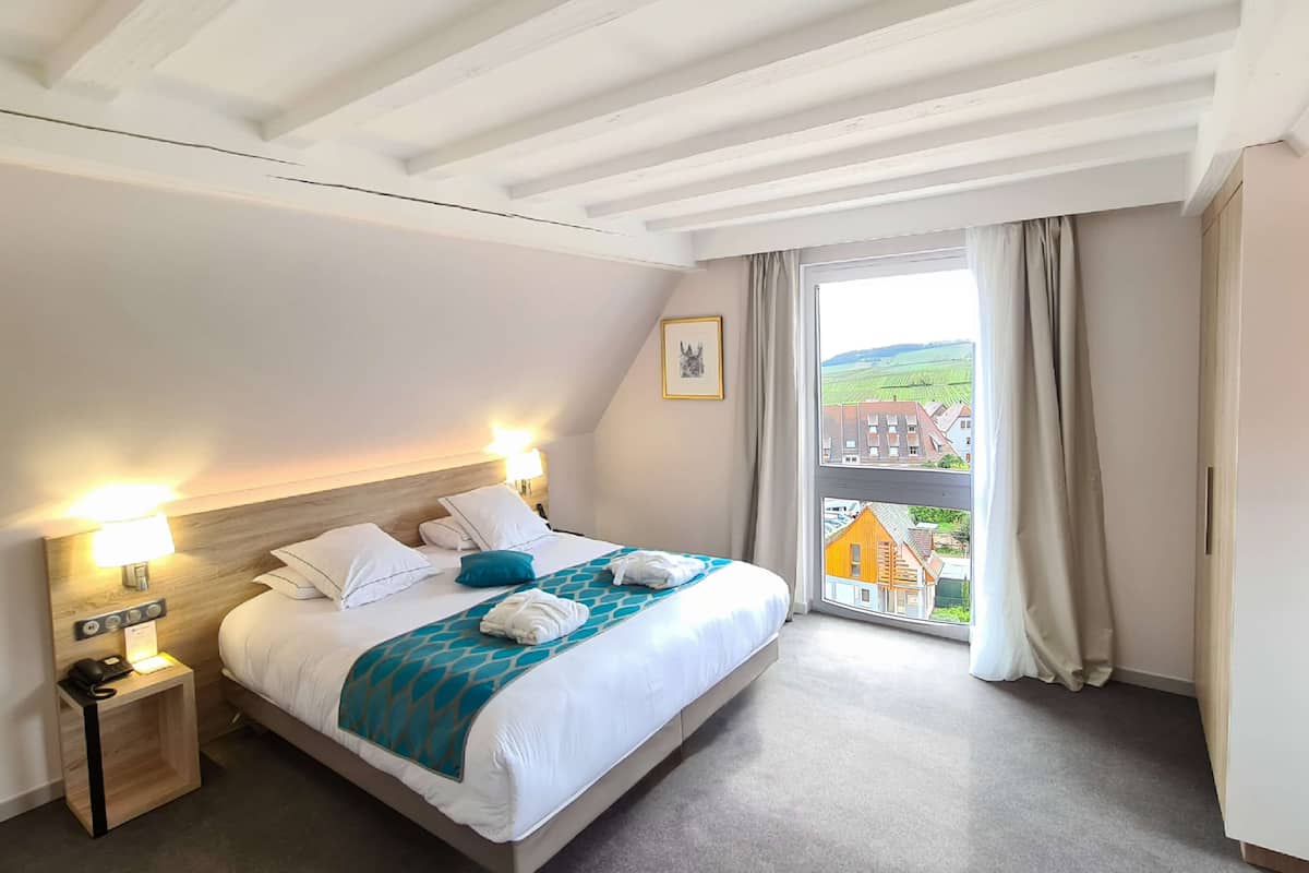 Ein Hotelzimmer mit Bett, Nachttischlampen, einem Nachttisch, einem Fenster mit Blick auf Gebäude und einem Vorhang.