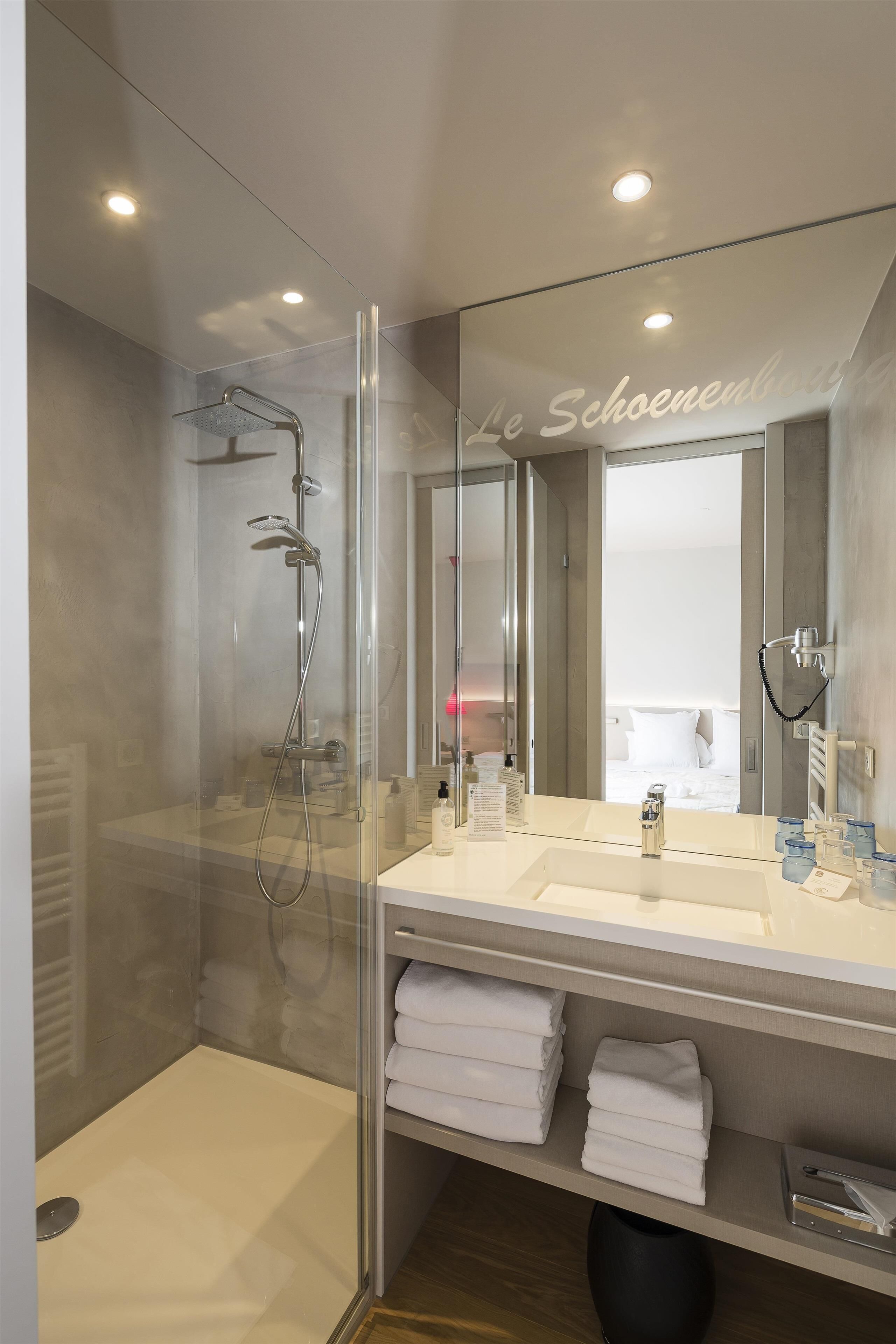 A modern bathroom with a glass-enclosed shower, a large mirror, and neatly folded towels on a shelf.