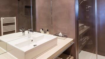 Un baño moderno con un lavamanos grande de color blanco, cabina de ducha de vidrio y un perchero para toallas.