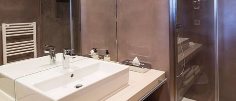 A modern bathroom with a large white sink, a glass shower enclosure, and a towel rack.