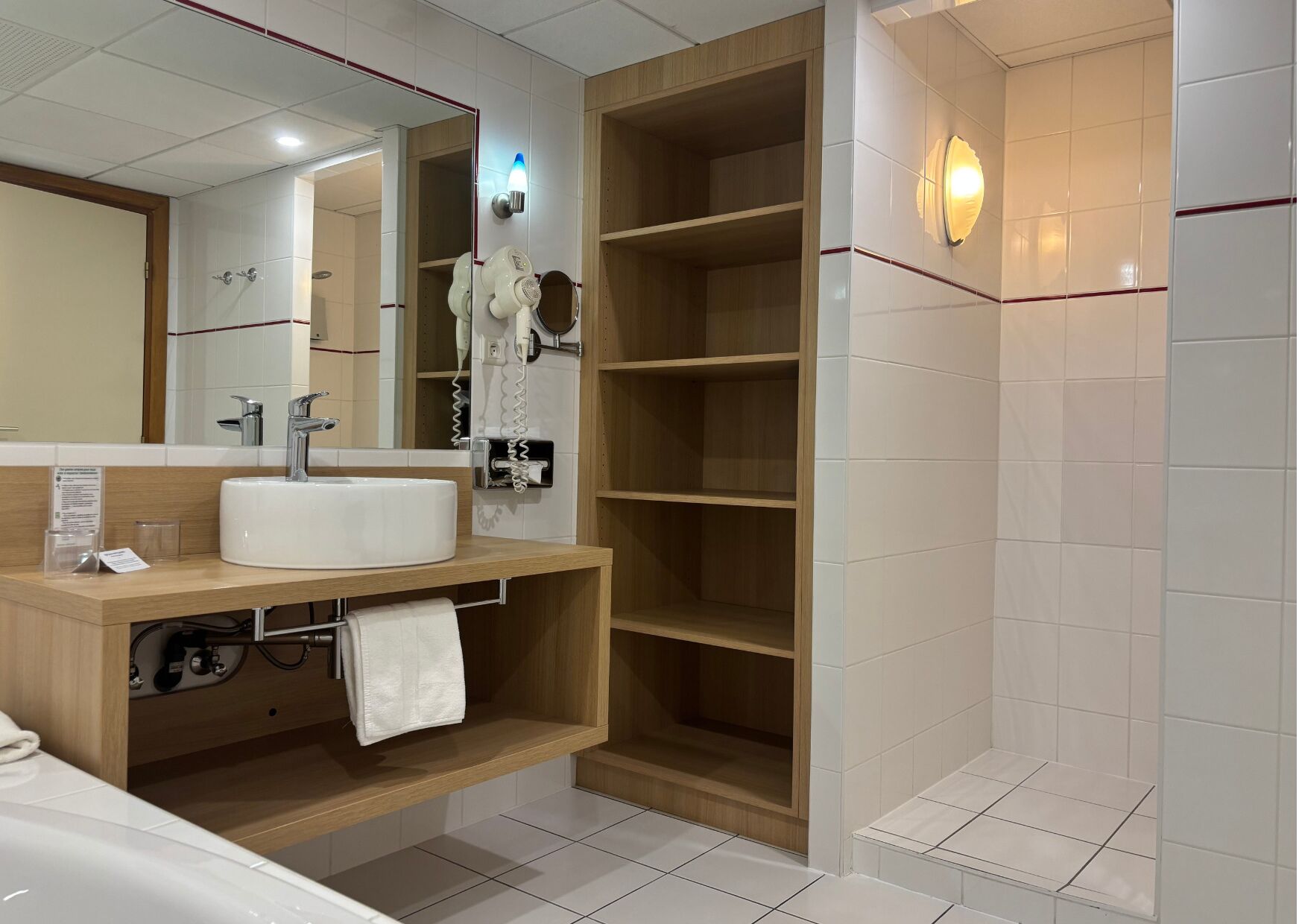 A modern bathroom with a white sink, a mirror, a towel rack, and a built-in shower stall.