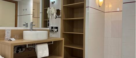 A modern bathroom with a white sink, a mirror, a towel rack, and a built-in shower stall.