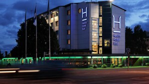 Un moderno edificio de hotel con un llamativo letrero en forma de 'H', varios pisos y una entrada bien iluminada.