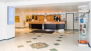 Zona de recepción de un hotel con diseño moderno, que incluye un mostrador de recepción, un reloj y una exhibición de varios objetos.