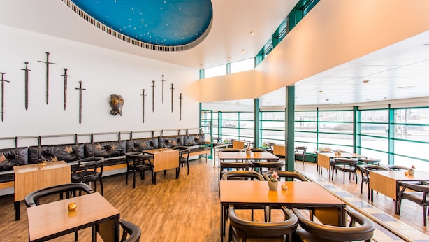 Un restaurante con techo alto, suelo de madera y una zona de estar con mesas y sillas.