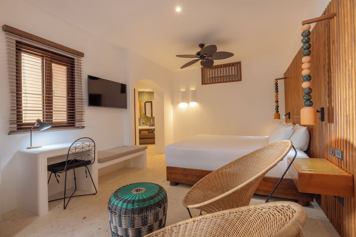 Ein Schlafzimmer mit einem Bett, einem Schreibtisch, einem Sessel, einem Deckenventilator und einem an der Wand befestigten Fernseher.
