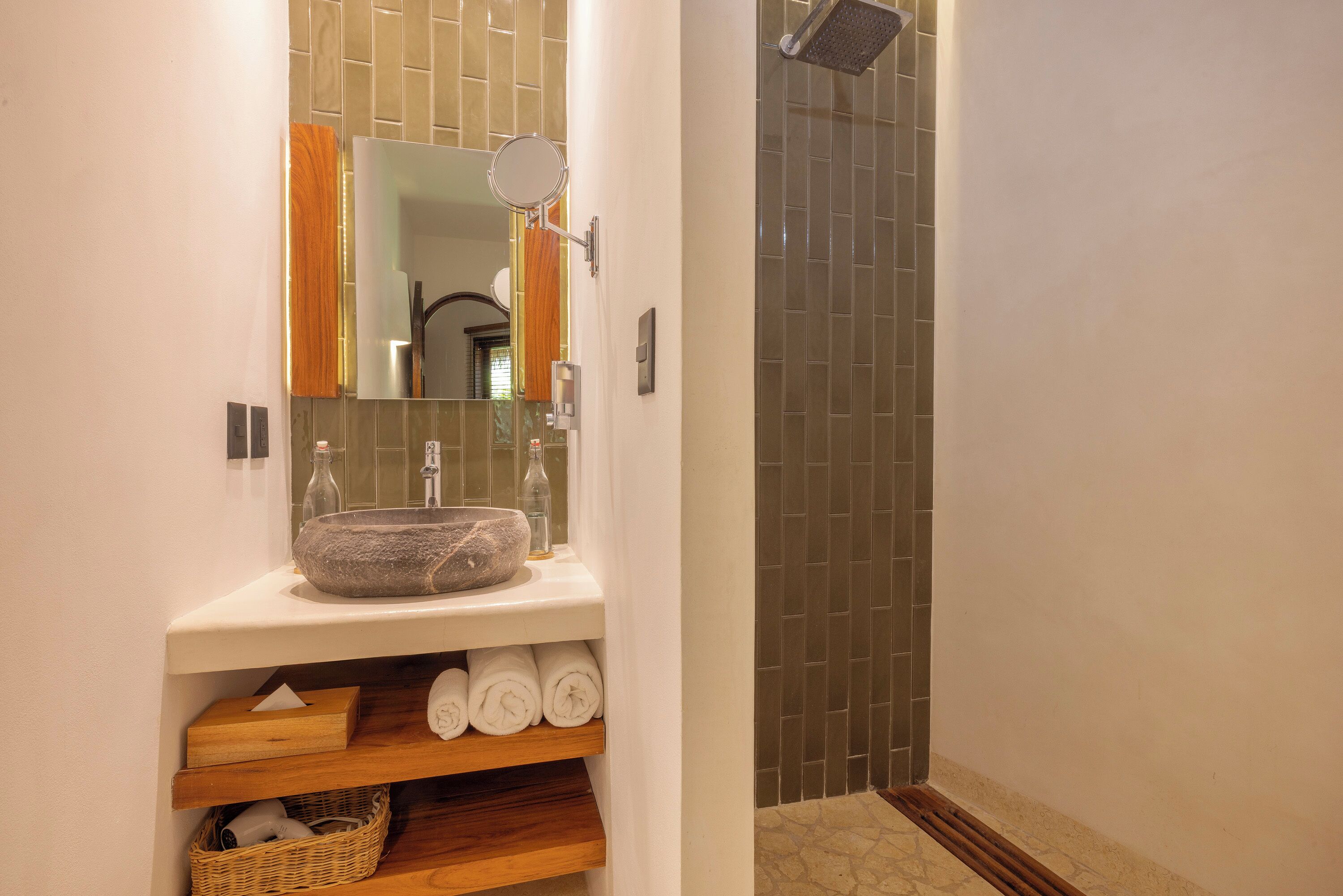 Une salle de bain avec un lavabo en pierre, un miroir, une douche aux carreaux foncés et des serviettes soigneusement rangées.