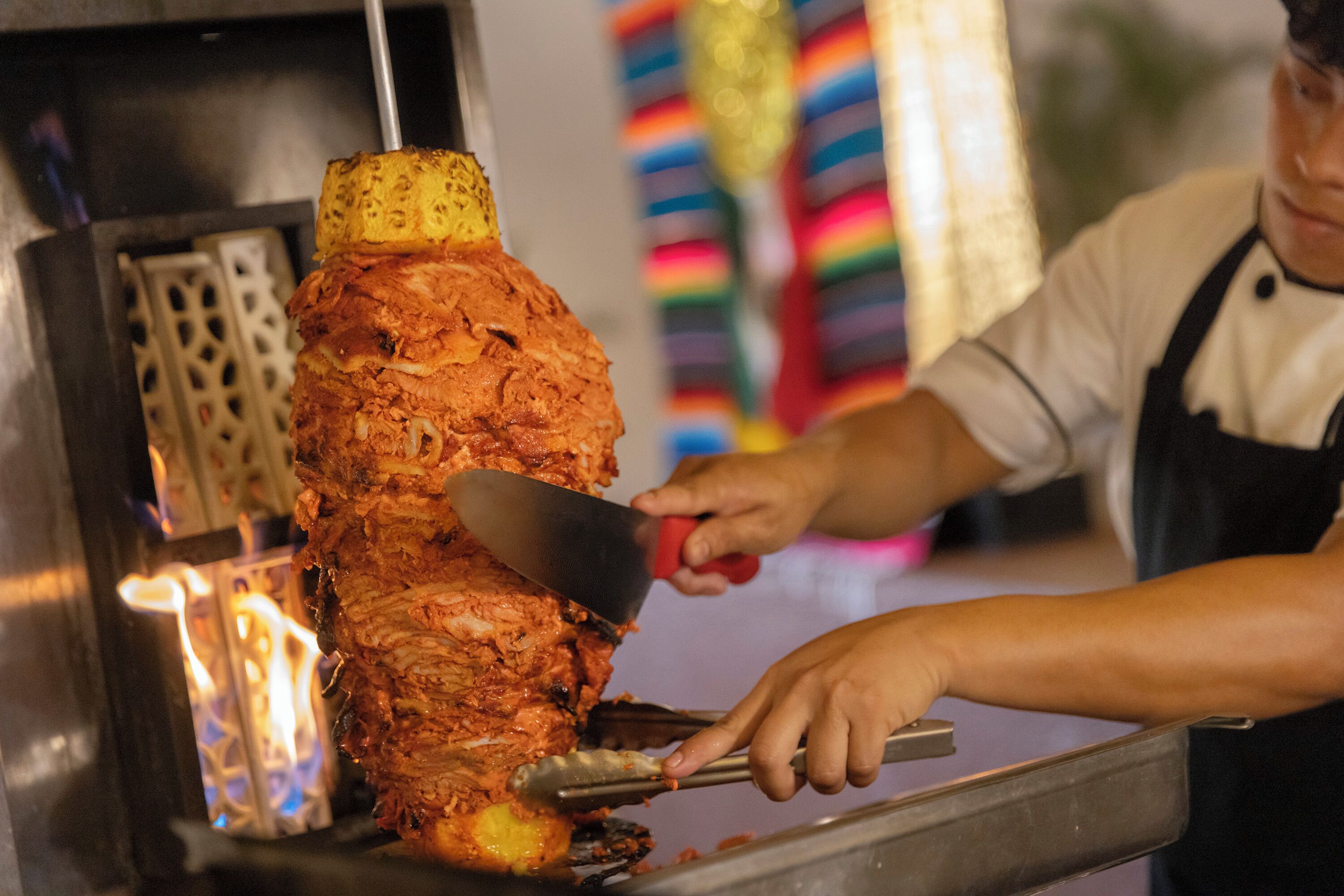 A person carving meat from a vertical rotisserie.
