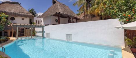 Una piscina con una estructura de techo de paja, un muro blanco y palmeras.