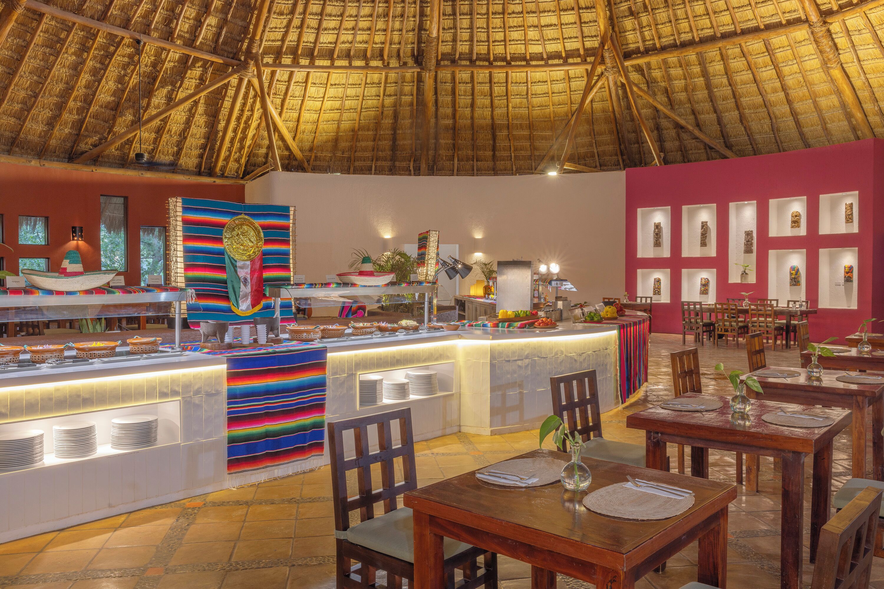 Un restaurante con techo de paja, pared a rayas coloridas y una zona de bar con una exhibición de platos y cuencos.