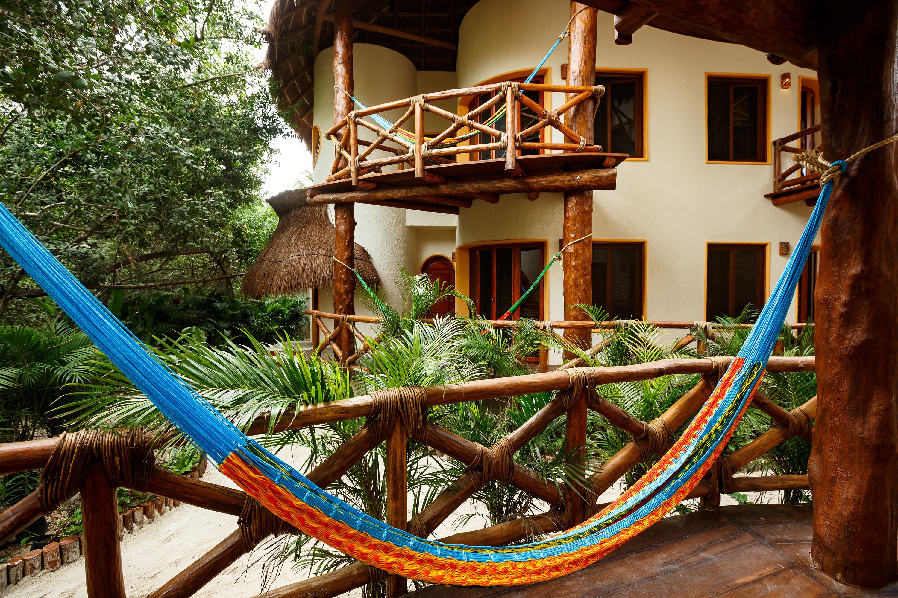 A hammock strung between wooden beams in a lush garden area with a building in the background.